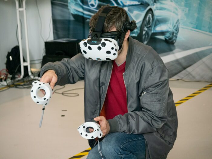 A man in a jacket and blue denim jeans with white and black panda VR headset and controllers