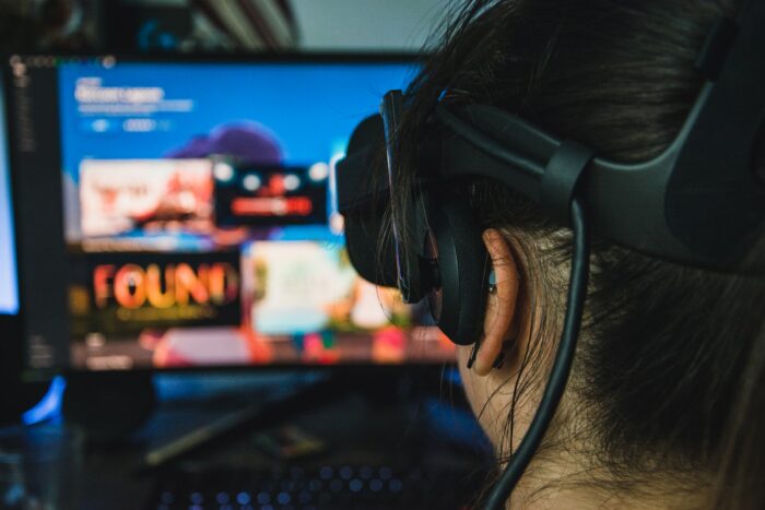 person wearing black VR metaverse headset in front of black flat screen computer monitor